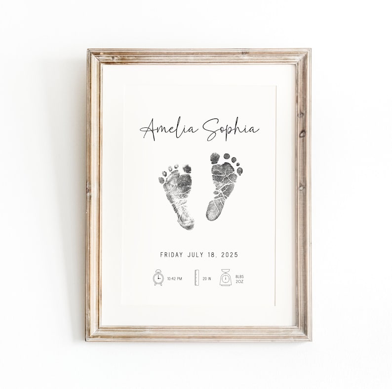 May include: A framed print with a black and white baby footprint design. The print includes the name "Amelia Sophia", the date "Friday July 18, 2025", and the time "10:42 PM".