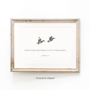 May include: A framed art print with two ducks in flight. The print includes the text "EVERY GOOD AND PERFECT GIFT IS FROM ABOVE" and "JAMES 1:17". The frame is a light brown colour, and the print has a minimalist design.