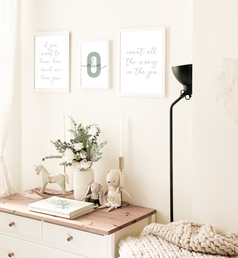 May include: Three white framed prints on a white wall. The left print says "If you want to know how much we love you". The middle print has a green number "0" with the name "Oliver" written in cursive. The right print says "Count all the waves in the sea".