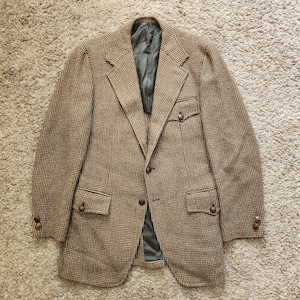May include: A brown and white tweed blazer with a single button closure and flap pockets. The blazer has a brown lining and brown buttons.