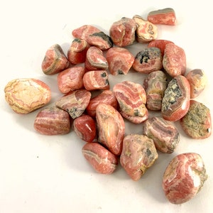 May include: A collection of pink and white striped tumbled stones. The stones are smooth and polished, with a variety of shapes and sizes.