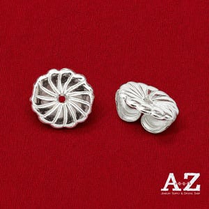 Peut inclure: Deux fermoirs de boucles d'oreilles de couleur argentée avec un bord festonné en forme de fleur et une ouverture circulaire centrale. Un fermoir est vu de dessus, tandis que l'autre est incliné pour montrer sa structure latérale incurvée.