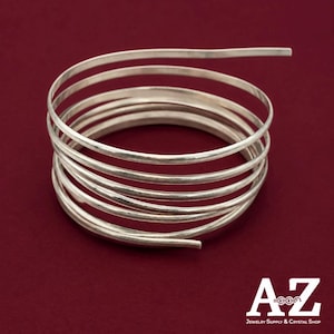 May include: A silver-colored metal wire coiled into a multi-layered spiral shape. The wire has a smooth, reflective surface and is arranged in several concentric loops. The text AZ Jewelry Supply & Crystal Shop is visible in the corner.