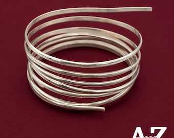 May include: A silver-colored metal wire coiled into a multi-layered spiral shape. The wire has a smooth, reflective surface and is arranged in several concentric loops. The text AZ Jewelry Supply & Crystal Shop is visible in the corner.
