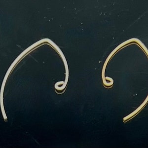Puede incluir: Cuatro pendientes de alambre de color dorado con un diseño curvo simple. Los pendientes tienen todos la misma forma, pero son de tamaños ligeramente diferentes.