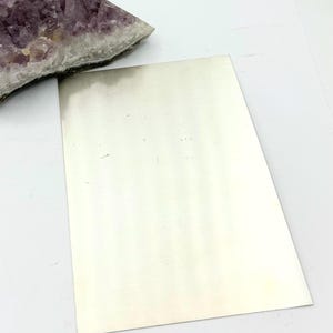 Puede incluir: Una l&aacute;mina de metal plateado, con una superficie lisa y brillante.