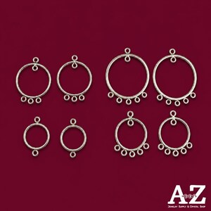 Könnte beinhalten: Eine Sammlung von acht kreisförmigen Schmuckverbindern aus silberfarbenem Metall, angeordnet in zwei Reihen. Die Teile weisen eine unterschiedliche Anzahl kleiner Ösen auf, die oben und unten an jedem Ring befestigt sind. Der Text AZ Jewelry Supply & Crystal Shop ist zu sehen.