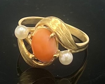 Può includere: Un anello d'oro con una pietra di corallo e due perle. L'anello ha un design attorcigliato.