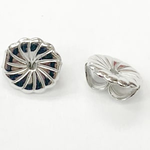 May include: Two silver earring backs with a decorative, scalloped design. The backs are designed to fit over the post of an earring.