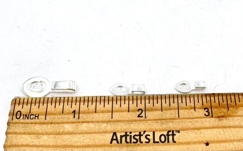 May include: Close-up of five clear plastic clasps for jewelry making, measured on a ruler with the text "Artist's Loft" in inches.
