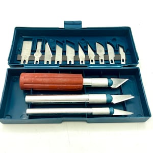 May include: A blue plastic case with a set of 12 silver utility knives and three replacement blades. The case has a red handle and a silver blade.