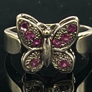 Può includere: Un anello d'argento con un design a farfalla. La farfalla ha pietre preziose rosa sulle ali.