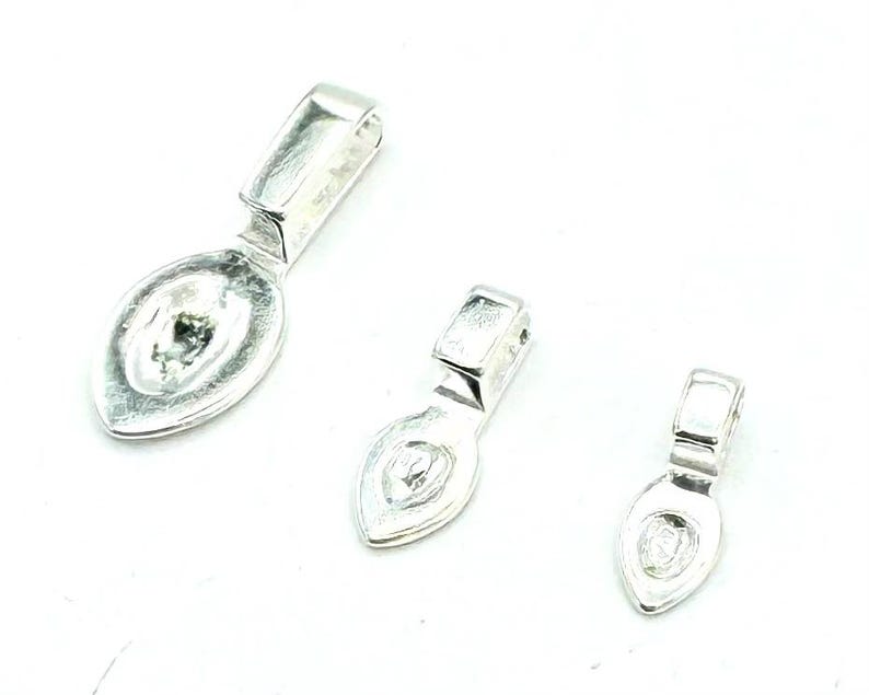 May include: Three silver-toned pendant bails in different sizes. The bails are shaped like a teardrop with a flat, oval-shaped top.