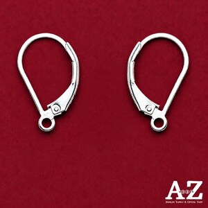 May include: A pair of silver-toned metal earring findings featuring a leverback closure mechanism. Each component has a rounded, teardrop-shaped wire loop and a small circular ring at the base for attaching jewelry elements, presented against a red background.