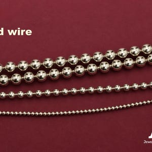 Peut inclure: Trois brins de fil à perles à billes argentées de diamètres variés disposés horizontalement. Le texte "Bead wire" apparaît dans le coin supérieur gauche, et le logo "AZ Jewelry Supply & Crystal Shop" est dans le coin inférieur droit.