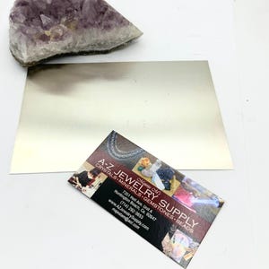 Puede incluir: Una tarjeta de visita para A-Z Jewelry Supply, con un fondo rojo y texto blanco. La tarjeta incluye el nombre de la empresa, la direcci&oacute;n, el n&uacute;mero de tel&eacute;fono, el sitio web y la direcci&oacute;n de correo electr&oacute;nico. La tarjeta tambi&eacute;n incluye una peque&ntilde;a imagen de una variedad de cristales y piedras preciosas.