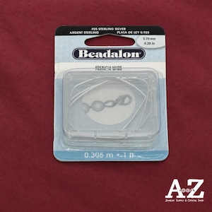 Könnte beinhalten: Eine Packung mit .925 Sterlingsilber-Draht von Beadalon. Der durchsichtige Kunststoffbehälter enthält den Silberdraht, und die Verpackung zeigt den Text .925 sterling silver, 0.70 mm und 0.305 m auf einem hellblauen Hintergrund.