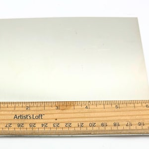 Puede incluir: Una l&aacute;mina de metal rectangular blanca que mide 15,2 cm por 10,2 cm. La l&aacute;mina de metal es lisa y tiene un ligero brillo.