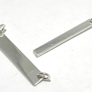 May include: Two silver metal bar pendants with jump rings. One bar is longer and the other is shorter.