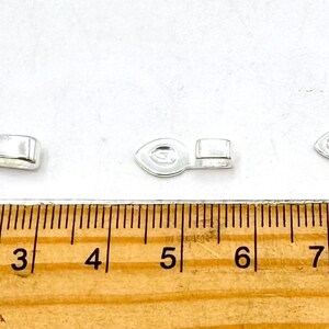 May include: Three silver-toned metal jewelry clasps of different sizes. The clasps are shown against a white background with a wooden ruler for scale.