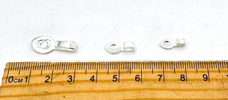 May include: Three silver-toned metal jewelry clasps of different sizes. The clasps are shown against a white background with a wooden ruler for scale.