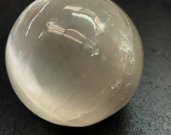 Op de afbeelding: Een gladde, witte selenietbol met een doorschijnende uitstraling. De bol heeft een licht troebele, melkachtig witte kleur en is gepolijst tot een hoge glans.