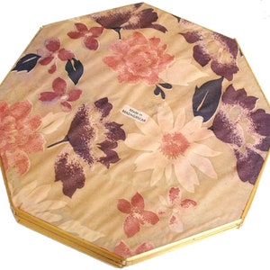May include: Octagonal, gold-framed mirror with a floral pattern on the back. The pattern is in shades of pink, brown, and white. The back of the mirror has a label that reads "Made in MADAGASCAR".