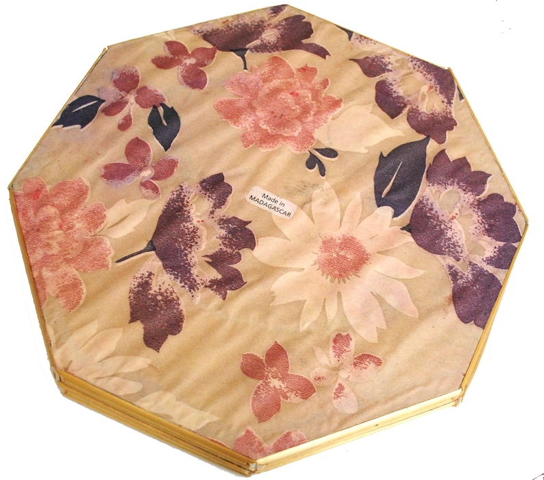May include: Octagonal, gold-framed mirror with a floral pattern on the back. The pattern is in shades of pink, brown, and white. The back of the mirror has a label that reads "Made in MADAGASCAR".