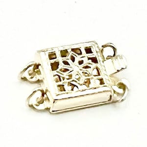 May include: Silver-toned metal clasp with a decorative, openwork design. The clasp has two loops on each side for attaching a necklace or bracelet.
