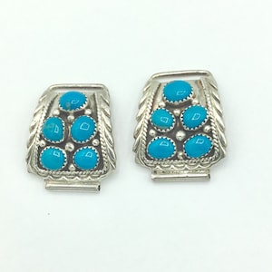 Op de afbeelding: Een paar zilveren horlogebandgespen met turquoise stenen. De gespen zijn ingewikkeld ontworpen in een southwestern stijl.