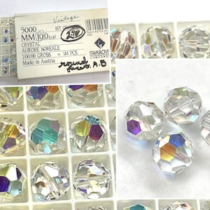 May include: A close-up of 144 clear crystal beads with an iridescent finish. The beads are 10mm in diameter and are packaged in a clear plastic container. The label on the container reads "5000 MM 10,0 mm 1ST QUALITY CRYSTAL AURORE BOREALE 1/00/00 GROSS = 144 PCS. Made in Austria."