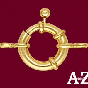 May include: A polished yellow gold spring ring clasp featuring a small spherical trigger knob at the top and two attached jump rings on either side. The metal surface is engraved with the text 14K. The letters A-Z are visible in the corner.