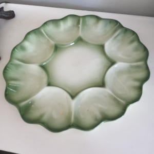 May include: A decorative, ceramic serving dish with a scalloped edge, resembling a flower or leaf. The dish features a central white area surrounded by green, petal-shaped compartments. The overall design is elegant and suitable for serving appetizers or snacks.