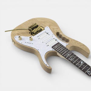 Unfinished natural wood electric guitar body of Ibanez Jem guitar with a white pickguard and gold hardware assembled. The guitar has a tremolo bridge and a single output jack.