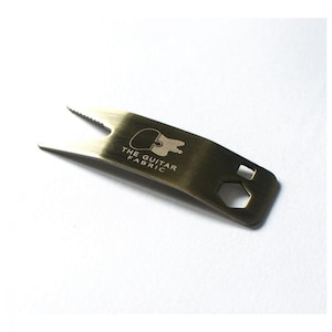May include: A gold-colored metal guitar tool with a  "THE GUITAR FABRIC" logo and multiple cutouts for different functions.