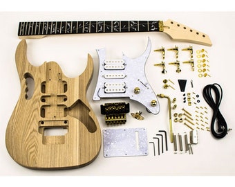 Könnte beinhalten: Unfertiger E-Gitarren-Bausatz mit einem Korpus aus natürlichem Holz, einem Ahornhals und verschiedenen Hardware-Komponenten. Enthält ein weißes Schlagbrett, einen schwarzen Tremolo-Steg und goldfarbene Stimmwirbel und Schrauben. Ein schwarzes Kabel ist ebenfalls enthalten.