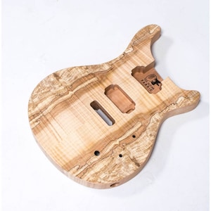 May include: Unfinished natural wood electric guitar body with a unique wood grain pattern. The body is shaped like a traditional electric guitar with a cutaway for access to the higher frets. The body is labeled "The Guitar Fabric".