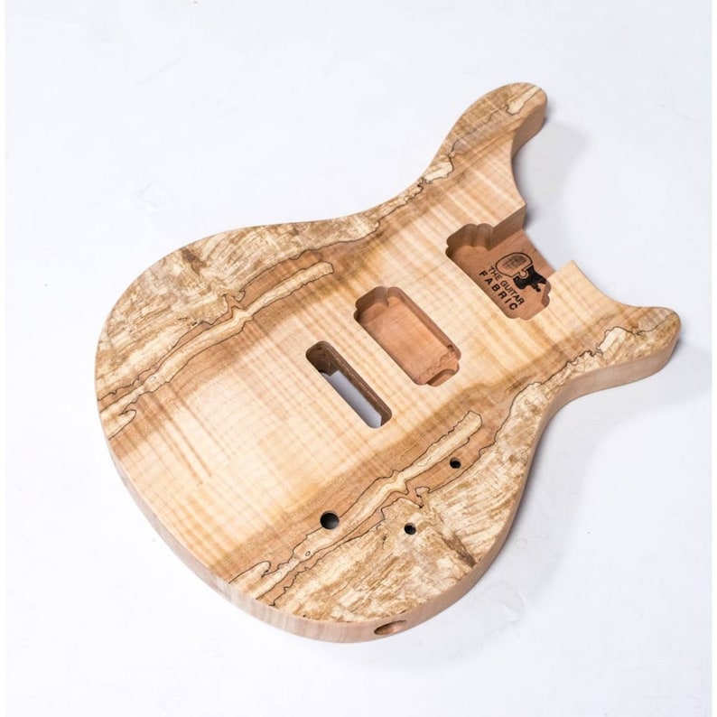 May include: Unfinished natural wood electric guitar body with a unique wood grain pattern. The body is shaped like a traditional electric guitar with a cutaway for access to the higher frets. The body is labeled "The Guitar Fabric".