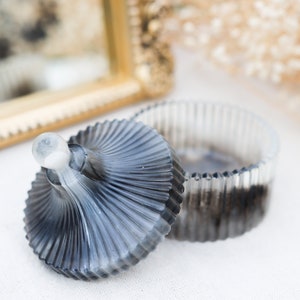 Puede incluir: Un tarro de vidrio negro y blanco con un diseño acanalado y una tapa a juego. La tapa tiene un pomo en la parte superior.