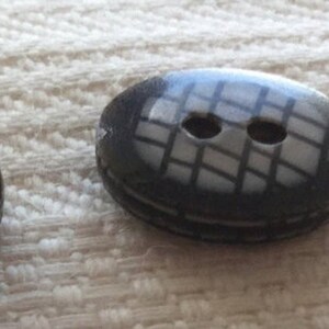 Puede incluir: Dos botones negros con dos agujeros cada uno. Un botón tiene un patrón a cuadros, el otro es sólido.