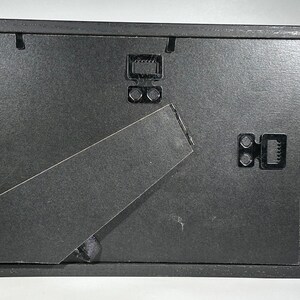 May include: Black picture frame with a black easel stand on the back. The frame has two black metal hanging hooks on the back.
