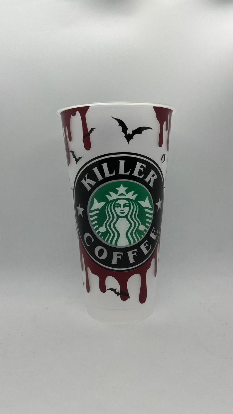 May include: White reusable cup with a red dripping blood design. The cup has a black and white graphic of a Starbucks logo with the text "Killer Coffee" around it. There are also black bats on the cup.
