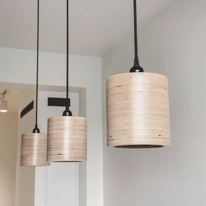 May include: Three wooden pendant lights with black cords hanging from the ceiling. The lights are cylindrical in shape and have a natural wood finish.