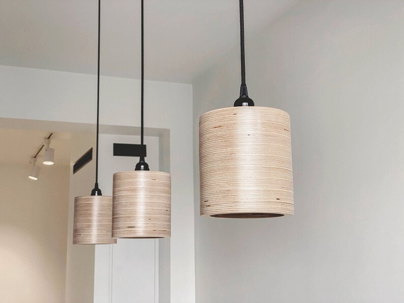 May include: Three wooden pendant lights with black cords hanging from the ceiling. The lights are cylindrical in shape and have a natural wood finish.