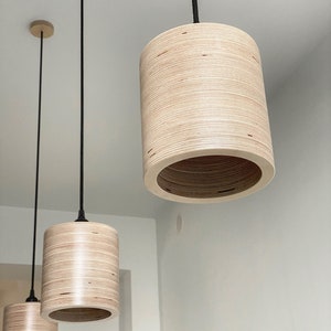 May include: Three pendant lights with wooden shades hanging from black cords. The shades are made of light brown plywood and have a cylindrical shape.