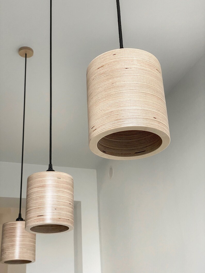 May include: Three pendant lights with wooden shades hanging from black cords. The shades are made of light brown plywood and have a cylindrical shape.