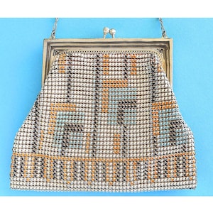 May include: Vintage metal mesh handbag with a silver frame and chain. The bag features a geometric pattern in white, orange, black, and light blue. The clasp is a silver tone. A classic accessory.