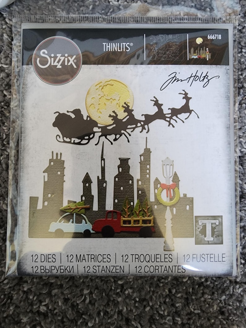 K&ouml;nnte beinhalten: Ein Sizzix Thinlits-Stanzformen-Set mit einer Stadtlandschaft, &uuml;ber der der Weihnachtsmann in seinem von Rentieren gezogenen Schlitten fliegt. Das Stanzformen-Set enth&auml;lt 12 Stanzformen, 12 Matrizen, 12 Troqueles, 12 Fustelle, 12 вырубки, 12 Stanzen und 12 Cortantes. Das Stanzformen-Set wurde von Jim Holtz entworfen.