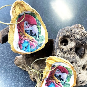 May include: Two gold-painted oyster shells with a colorful macaw bird image inside. Each shell has a gold string attached for hanging.