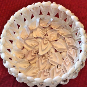 May include: A white seashell bowl with a decorative design. The bowl is made of many small seashells that are arranged in a circular pattern. The bowl is perfect for holding small items, such as jewelry or keys.